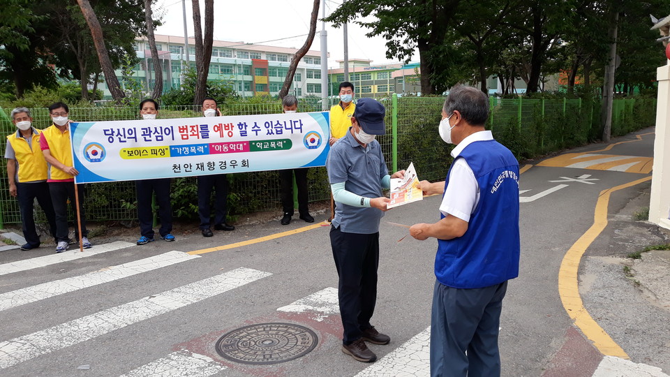 참수리봉사클럽 회원들이 범죄예방 현수막을 들고 전단지를 배포하는 모습 [사진=송기문]