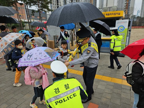   천안가람초등학교 정문, 등굣길  어린이들에게 홍보물을 배부하면서 교통안전 캠페인을 하고있다